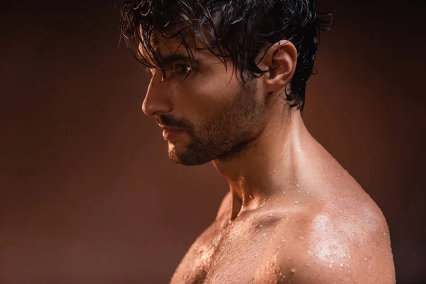 shirtless, wet man looking away while posing on dark background