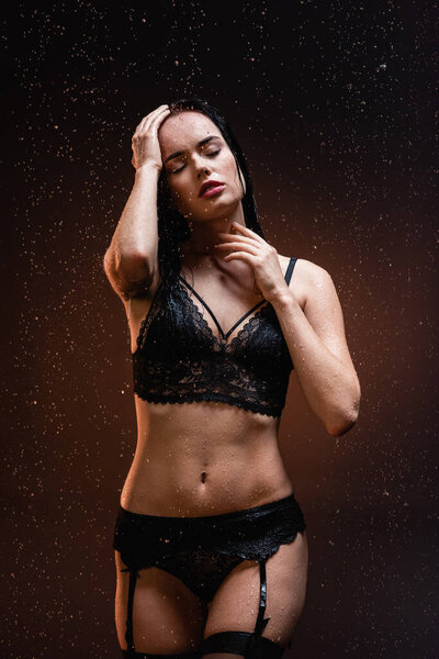 sexy woman in black lace underwear and stockings with closed eyes under falling raindrops on dark background