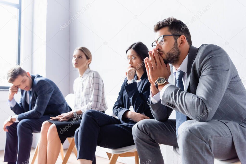 Businessman sitting near multiethnic employees on blurred background in hall in office 