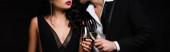 abgeschnittene Ansicht eines sexy Paares mit Champagnergläsern beim Anstoßen isoliert auf schwarz, Banner