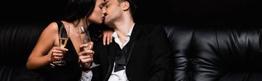 Kanepede oturmuş şampanya içerken öpüşen ve bardakları tutan seksi çift.
