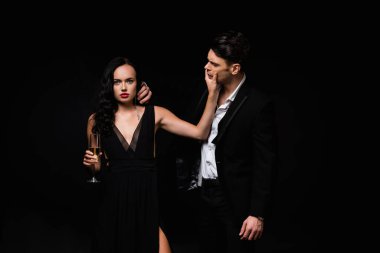 Elinde şampanya kadehi olan seksi bir kadın. Siyah giysili bir adamın yüzüne dokunuyor. 