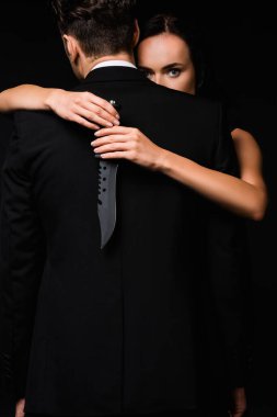 Siyah bir adamın sırtında bıçak tutan tehlikeli bir kadının kameraya baktığı kısmen görülüyor. 