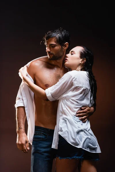 seductive woman taking off wet shirt from sexy man on dark background