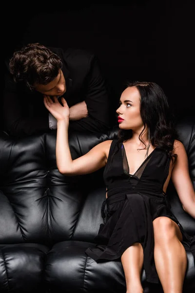 黒い服を着た女がソファに座り男の顔に触れる — ストック写真