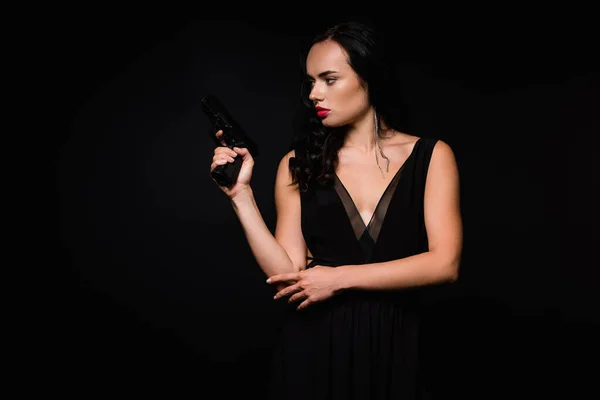 穿着连衣裙的黑发女人拿着枪隔离在黑暗中 — 图库照片