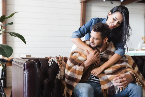 Glimlachende Brunette Vrouw Omarmen Vriendje Zitten Lederen Bank Onder Plaid — Stockfoto