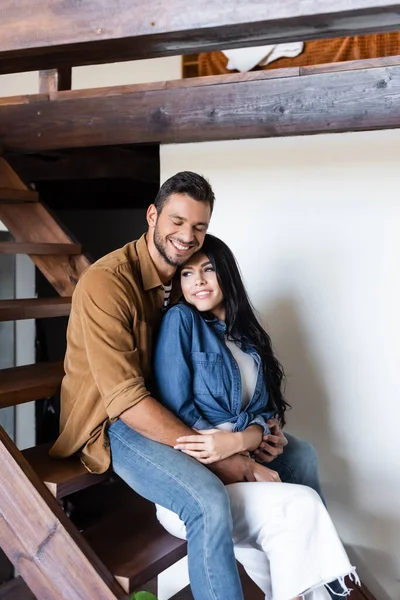 Young Couple Casual Clothes Smiling While Embracing Wooden Stairs Home — Stock Photo, Image