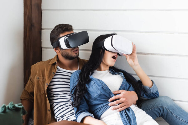 amazed woman touching vr headset while gaming together with boyfriend at home