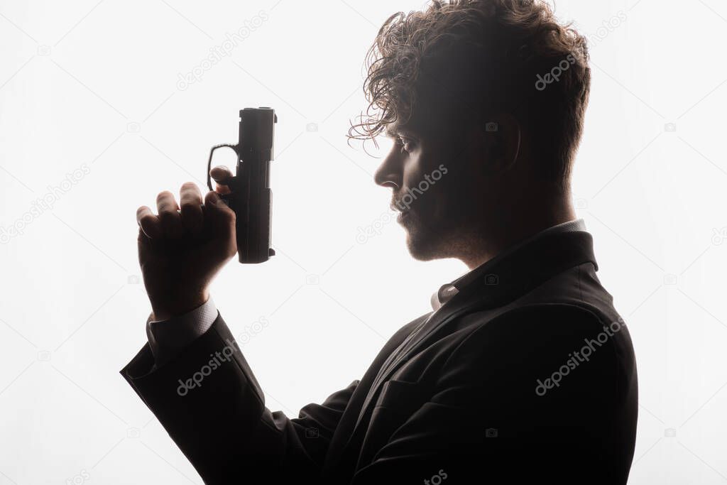 side view of curly man in formal wear holding gun isolated on white