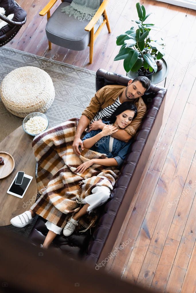 top view of young couple sleeping under cozy plaid blanket on leather couch in living room