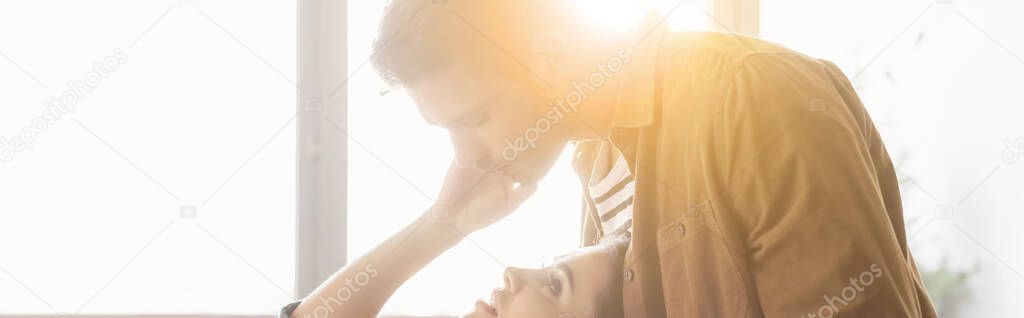 side view of man bending over woman touching his face in sunshine, banner