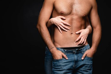Siyahta izole edilmiş seksi bir adamın kaslı gövdesini kucaklayan kadının kısmi görüntüsü