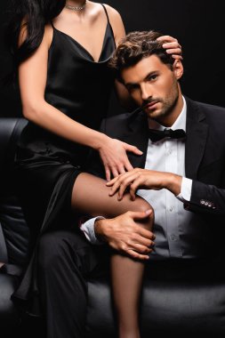 sexy woman in satin dress seducing elegant man in black suit isolated on black clipart