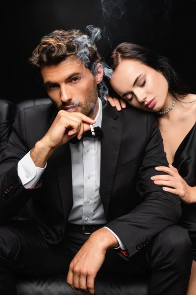 閉じた目をした官能的な女性巨大な肩のエレガントな男の喫煙と黒で隔離されたカメラを見て — ストック写真