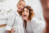 Mother and child sticking out tongues in bathroom  