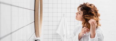 Kıvırcık kadın banyoda aynanın yanında saç ayarlıyor. 