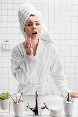 Havlulu, bornozlu, çenesine dokunan endişeli kadın. 