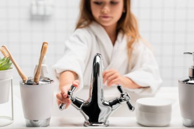 Girl opening water near toiletries and sink on blurred background  clipart