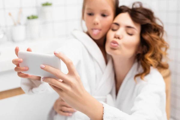 在浴室模糊的背景下 母亲和孩子摆出一副自拍的样子拿着智能手机 — 图库照片