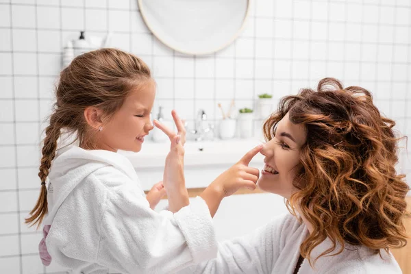 快乐的母亲和孩子在浴室的鼻子上涂化妆品霜 — 图库照片