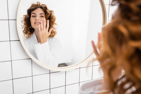 Mulher Sorridente Roupão Aplicando Creme Facial Perto Espelho Primeiro Plano — Fotografia de Stock