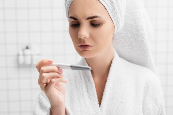 穿着浴衣的忧心忡忡的女人在现代浴室里看怀孕测试 — 图库照片