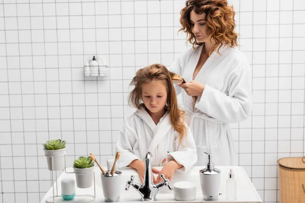 现代浴室里 女人在水槽边刷女儿的头发 — 图库照片