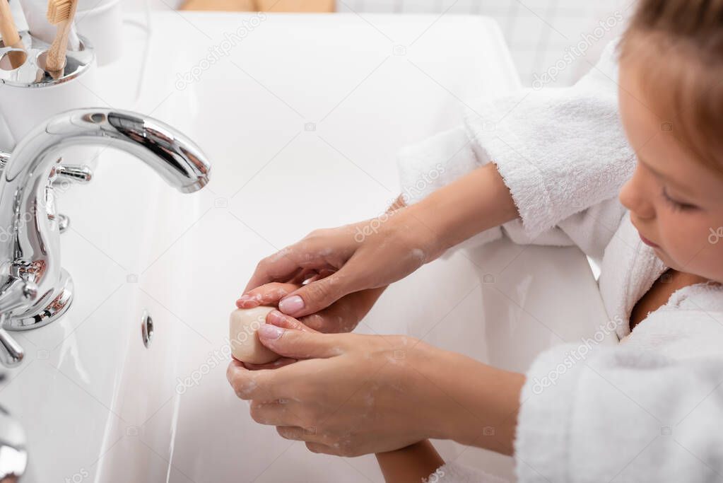 Mother and daughter washing hands near sink in bathroom 