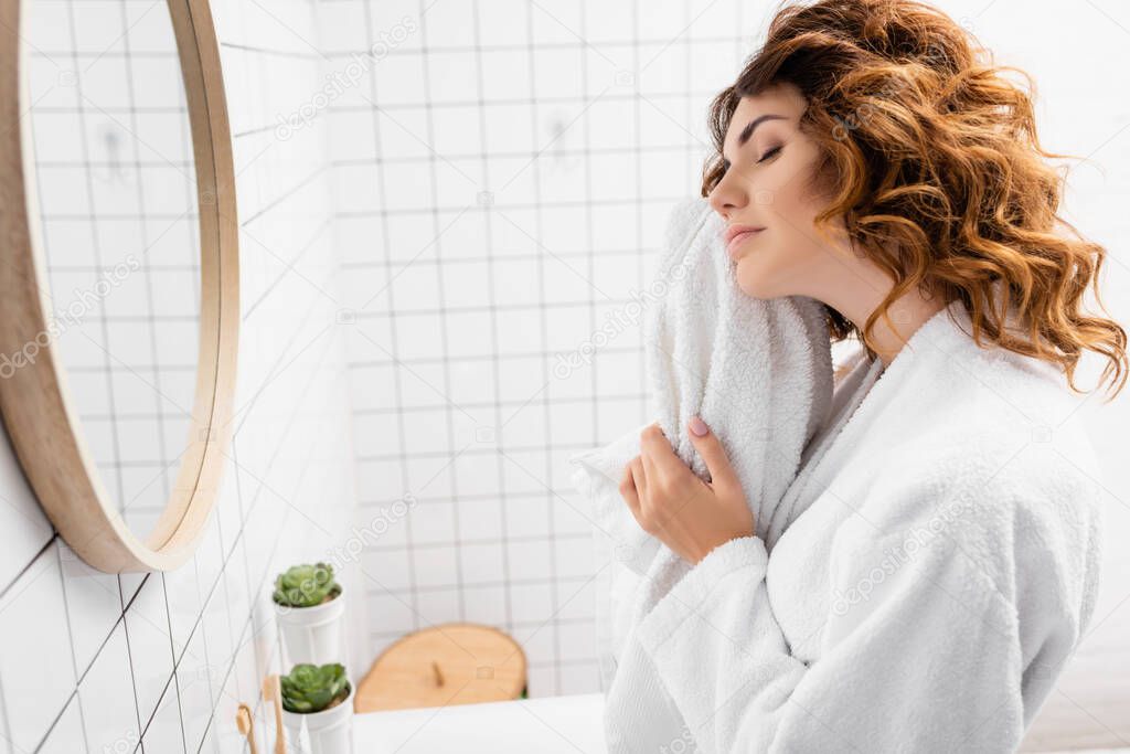 Curly woman holding white towel in bathroom 