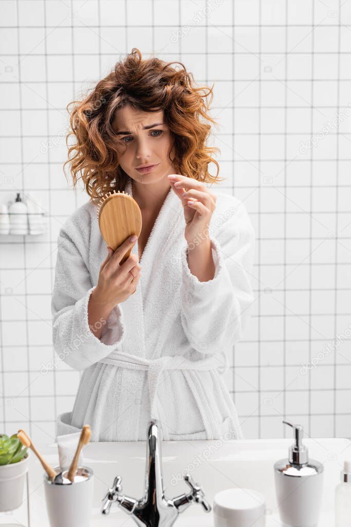 Disappointed woman holding hair brush in modern bathroom 