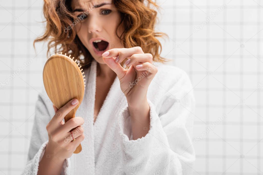 Hair brush in hand of amazed woman on blurred background in bathroom on blurred background