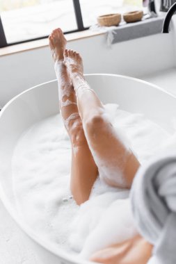 Legs of young woman in foam in bathtub on blurred foreground  clipart