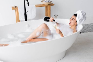 Pozitif kadın banyo yaparken kadehe şampanya dolduruyor. 