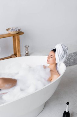Şampanya şişesinin yanında köpükle banyo yapan bir kadın. 