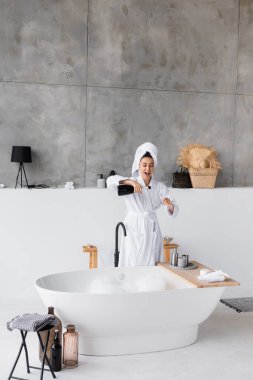 Neşeli kadın evinde küvetin yanında şampanyayı cama dolduruyor. 