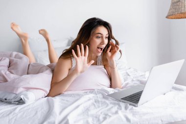 Neşeli kadın laptopta görüntülü sohbet yapıyor yatak odasındaki bulanık ön planda. 