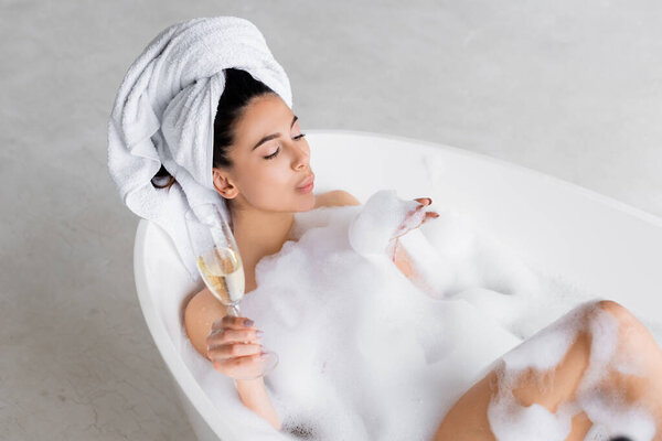 High angle view of woman blowing foam from hand while holding champagne glass in bathtub 