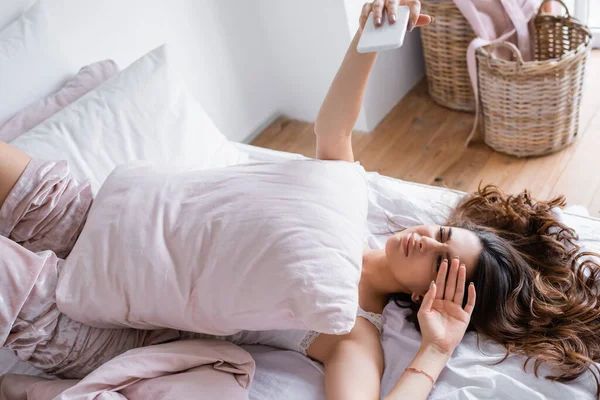 Pijamalı Bir Kadın Yatakta Akıllı Telefonuyla Selfie Çekiyor — Stok fotoğraf