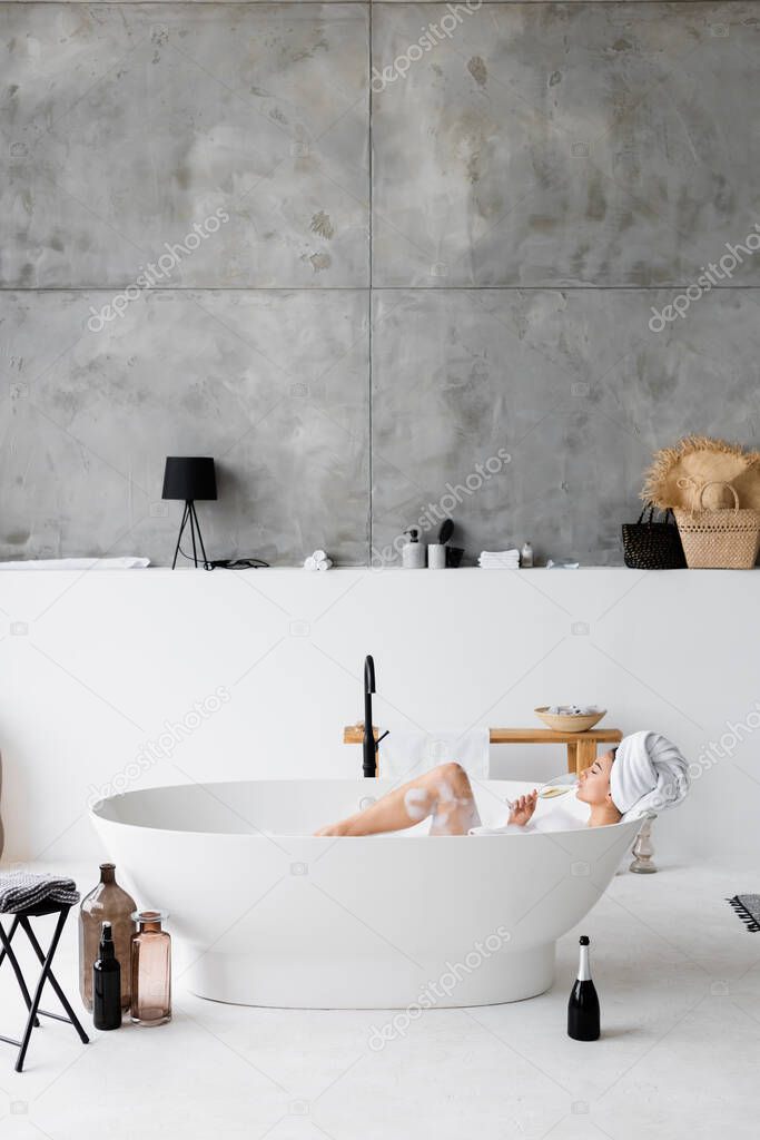 Young woman drinking champagne while taking bath with foam 