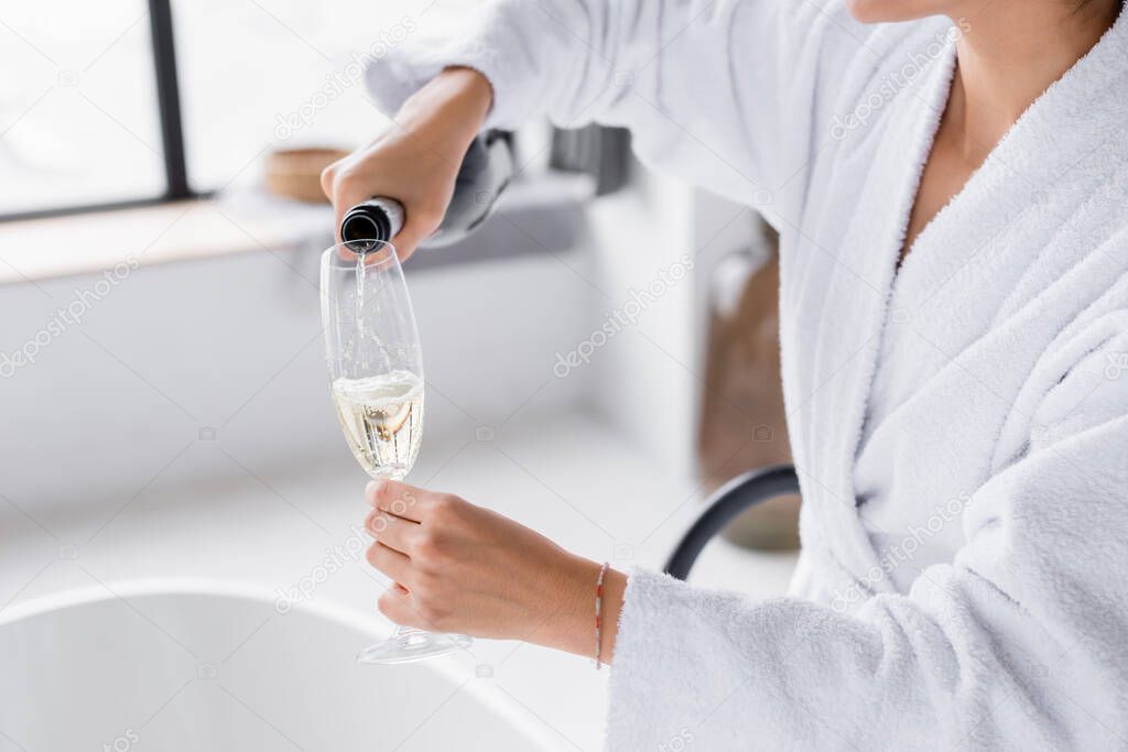 Cropped view of woman pouring champagne in glass in bathroom 