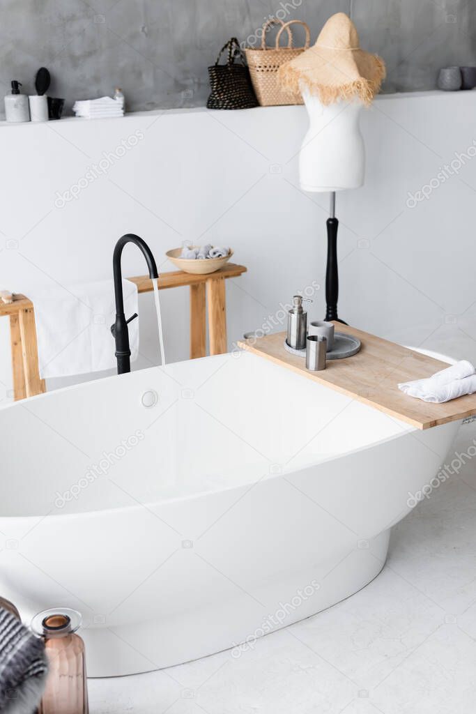 Toiletries on wooden tray on bathtub at home 