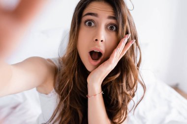 Heyecanlı bir kadın yatak odasındaki bulanık arka planda kameraya bakıyor. 
