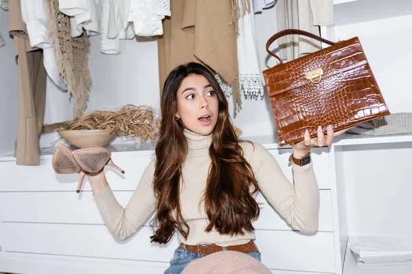 Young woman holding shoes and handbag in wardrobe