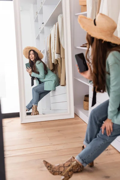 Mujer Sonriente Sombrero Sol Sosteniendo Teléfono Inteligente Cerca Del Espejo — Foto de Stock