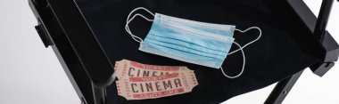 Sinema biletleri ve tıbbi maskeler siyah film yapımcısı sandalyesinde beyaz pankartta