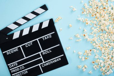 top view of clapperboard near popcorn scattered on blue, cinema concept clipart