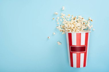 Çizgili karton kovanın mavi üzerine patlamış mısır, sinema konsepti.