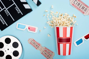 Alkış tahtası, 3D gözlükler, sinema biletleri, film makarası ve mavi üzerine patlamış mısır kovası.