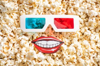top view of 3d glasses and paper cut smiling mouth on crispy popcorn, cinema concept clipart